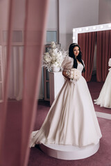 The bride in a white dress in front of the mirrors in the living room. Preparing for the upcoming wedding. Burgundy background.