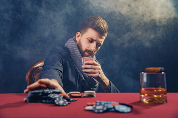 Beared man in suite is playing cards in a casino on red cloth on a table. Winner. Nut hand 