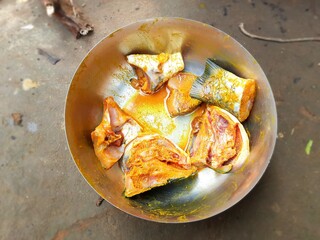 Raw fish pieces are ready for frying. Salt and turmeric have been mixed in it. The fish is kept in a vessel.