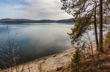 Autumn landscape with lake shore, trees, mountains and sky with clouds