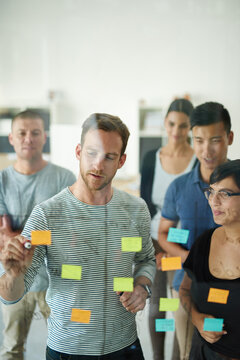 Planning is the first step. Cropped shot of a group of young designers planning on a glass board.
