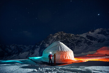 Man with snowboard near Yurt nomadic house at night at Mountains