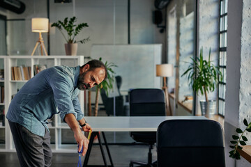 Middle adult man measures distances between desks in office