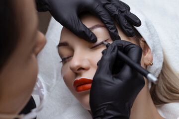 Permanent makeup. Cosmetologist tattoo artist applies a contour to the client's eyelid for...