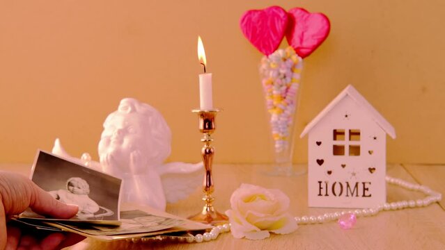 close-up female hand holding old vintage photos, romantic still life in love style, in vase red hearts on sticks, candles burning, cupid, concept of family tree, genealogy, childhood memories