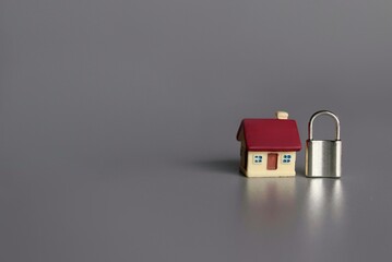 Home security concept. Toy house and padlock with copy space for text on grey background.