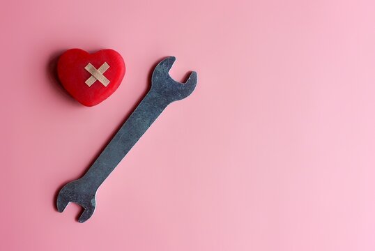 Fix, mend a broken heart concept. Red heart, bandage and spanner on pink background with copy space.