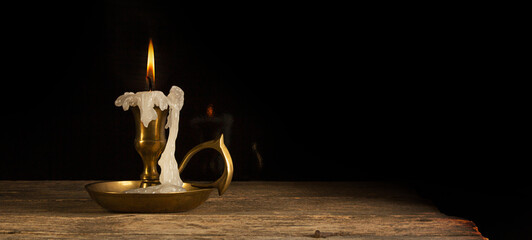 Candle in candlestick on the wooden table, vintage style, dark background.