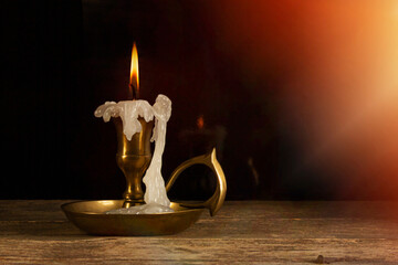 Candle in candlestick on the wooden table, vintage style, dark background, sunligt.