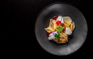 Crepes with strawberries jam and cream cheese on black plate on wooden table dark background