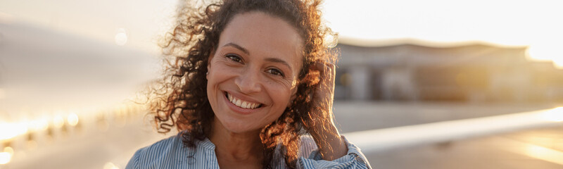 Portrait of happy female tourist, cheerful woman smiling at camera while standing outdoors ready...