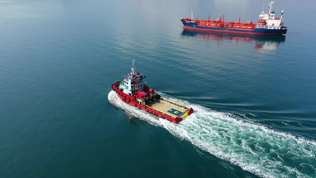 Aerial drone tracking video of assistive tug boat cruising in Mediterranean logistics port
