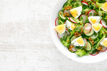 Easter fresh vegetable salad with boiled egg, radish and cucumber, dressing with dijon mustard and lemon on white wooden table. Top view