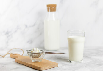 A glass of kefir and kefir grains on a strainer over a glass jar, standing on a wooden cutting...