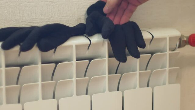 Drying winter clothes at home. A man puts wet winter gloves on a home heating radiator to dry. A man checks the heat energy from a heating battery.Selective focus
