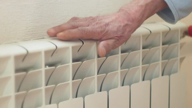 The hand of an elderly man touches a heating radiator, checking the heating temperature of heating appliances in the apartment. Heating dma in winter. Faulty central heating radiator. selective focus