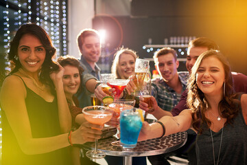 Heres to the good times. Portrait of a group of people toasting with their drinks at a nightclub.