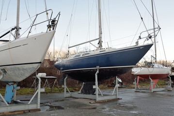 Blue sloop rigged sailboat standing on land in a yacht club. Service, repair, transportation,...