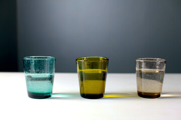 colorful glasses with water on a white table on a dark background
