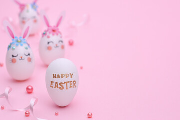 Pink Easter composition with copy space. Three white Rabbit Eggs with flowers, ears and muzzles on a pink background decorated with ribbons and beads. Golden Greeting text Happy Easter on a white egg.