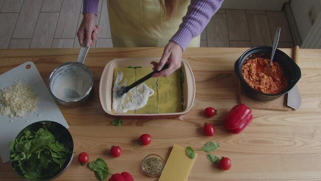 Woman is cooking tasty dinner at home, putting white sauce on lasagna noodles, preparing meal with love for her family, Slow motion.