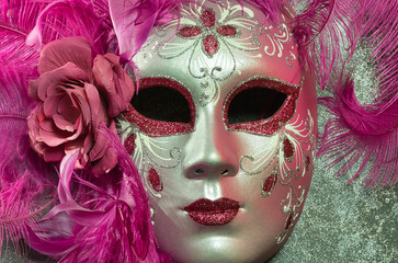 Carnival mask handmade in venice. The mask is made of papier-mâché and represents the face of a woman, is colored pink and decorated with feathers. The mask is a masterpiece of Venetian craftsmanship.
