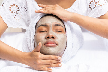 Fototapeta na wymiar American-African woman uses a mask and has a massage therapist give her a moisturized facial in a spa salon.