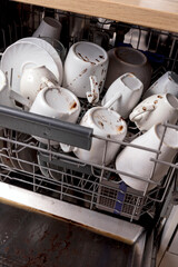 Unwashed, dirty dishes in dishwasher. Mess in the kitchen. Dirty kitchenware, plates and mugs. Messy dishware. Close up view.