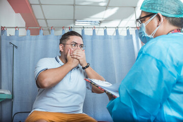A shocked male patient in his 30s covers his hand in disbelief from the bad diagnosis of a...