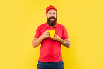 Happy bearded man in casual red cap and tshirt holding cup yellow background, tea