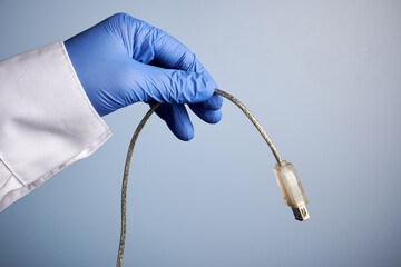Doctor hand holds USB cord - labs photo with blue background. Scientist palm offers USB cable connector. Student hand in blue nitrile glove. Network hardware for data transfer between computers.