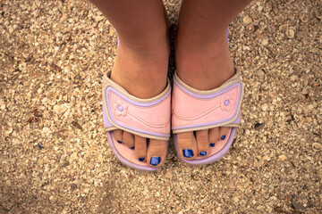 A woman in pink sandals stands on the beach. Women's feet in pink flip-flops stand on a shell beach