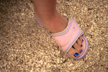 Women's feet in pink flip-flops stand on a shell beach