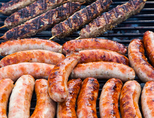 Sausages and minced meat on wooden sticks are cooked on the grill.