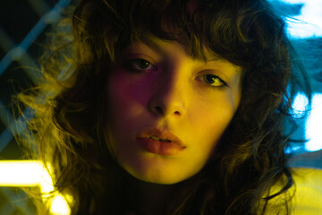 Fototapeta premium Portrait of a beautiful young woman with curly hair in neon lighting.