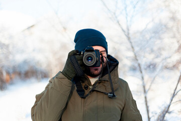 Fototapeta na wymiar A man in a winter hat and mittens shoots with a digital SLR camera while standing outdoors