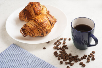 delicious, appetizing, crispy croissants, hot coffee in the blue cup and kitchen towel on plate on marble table
