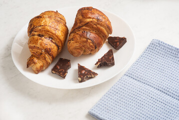 delicious, appetizing, crispy croissants with dark chocolate and kitchen towel on plate on marble table. French pastries