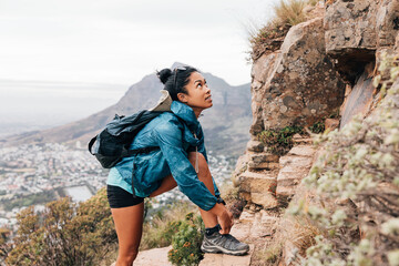 Woman in sports clothes tying shoelaces and looking up during hiking on a mountain