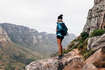Rear view of a woman with a backpack on a hike. Young female standing on a path enjoying the scenic view from the top.