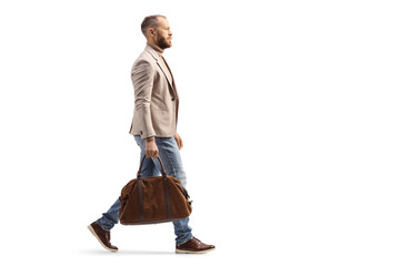 Full length profile shot of a man in a beige suit and jeans carrying a fashionable bag