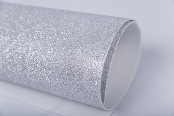 A roll of thick silver paper with glitter on a white background. Shiny fabric for creativity.