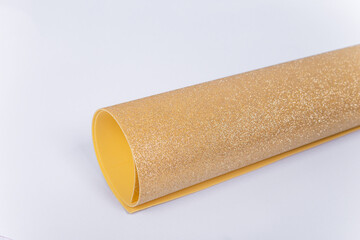 A roll of thick golden paper with sparkles on a white background. Shiny fabric for creativity.