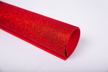 A roll of thick red paper with sparkles on a white background. Shiny fabric for creativity.