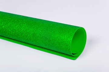 A roll of thick green paper with sparkles on a white background. Shiny fabric for creativity.