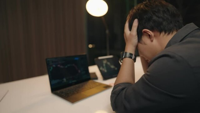 Young asian man feel disappointed after looking at trading charts, crypto currency trader on falling market, bear market, rug pull, liquidation of leverage future trading, fail sad evening