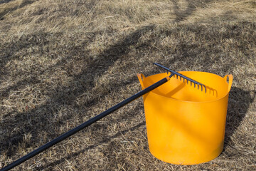 A yellow bucket and a black metal rake on grass