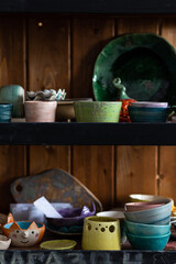 In the pottery. Assortment of handmade ceramic cups, mugs, bowls on wooden shelf
