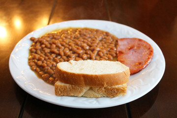 Close-up of a plate of baked beans with ham and a slice of bread.
