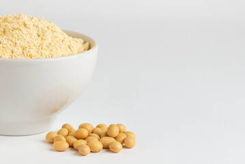 Fragment of white ceramic bowl with soy flour and soybeans on a white background with copy space